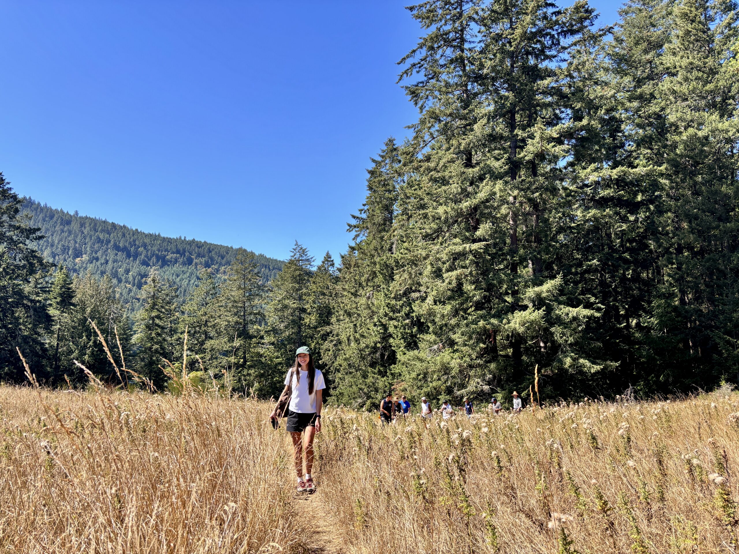 Josie Iaci stands in the middle of a yellow below in front of REFBC and Stqeeye team members walking in Xwaaqwu'um (Bourgogne Bay Provincial Park, Salt Spring Island0